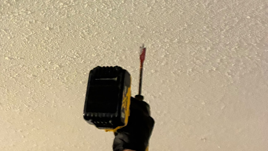 Gloved hand holding a moisture meter against a textured ceiling during field moisture mapping